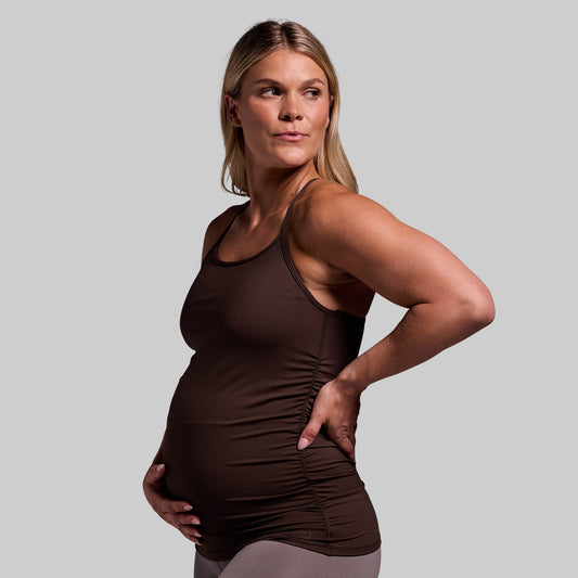 A pregnant woman wearing a dark brown maternity drop shot tank top with a built-in bra layer.