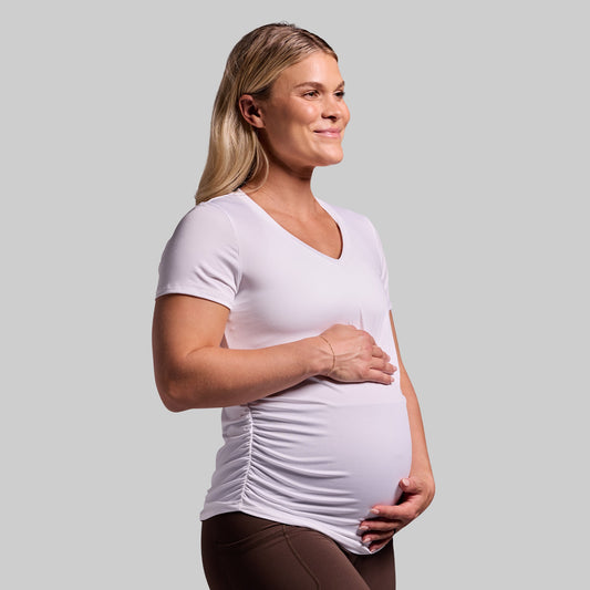 A pregnant woman wearing a white short sleeve v-neck top with ruched sides.