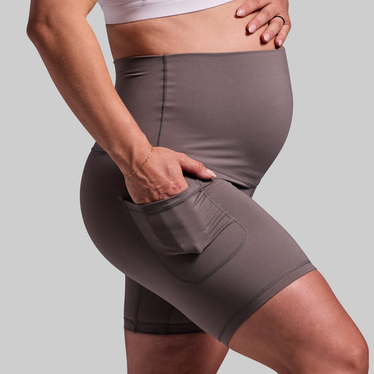 A pregnant woman wearing a pair of grey maternity biker shorts with pockets.