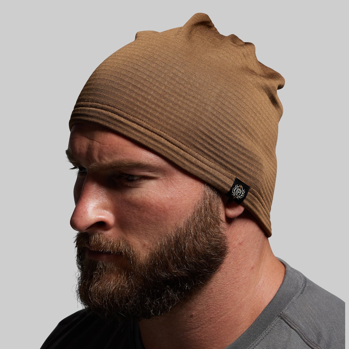 Man wearing a brown beanie with a brand logo on a gray background