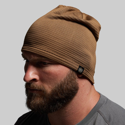 Man wearing a brown beanie with a brand logo on a gray background