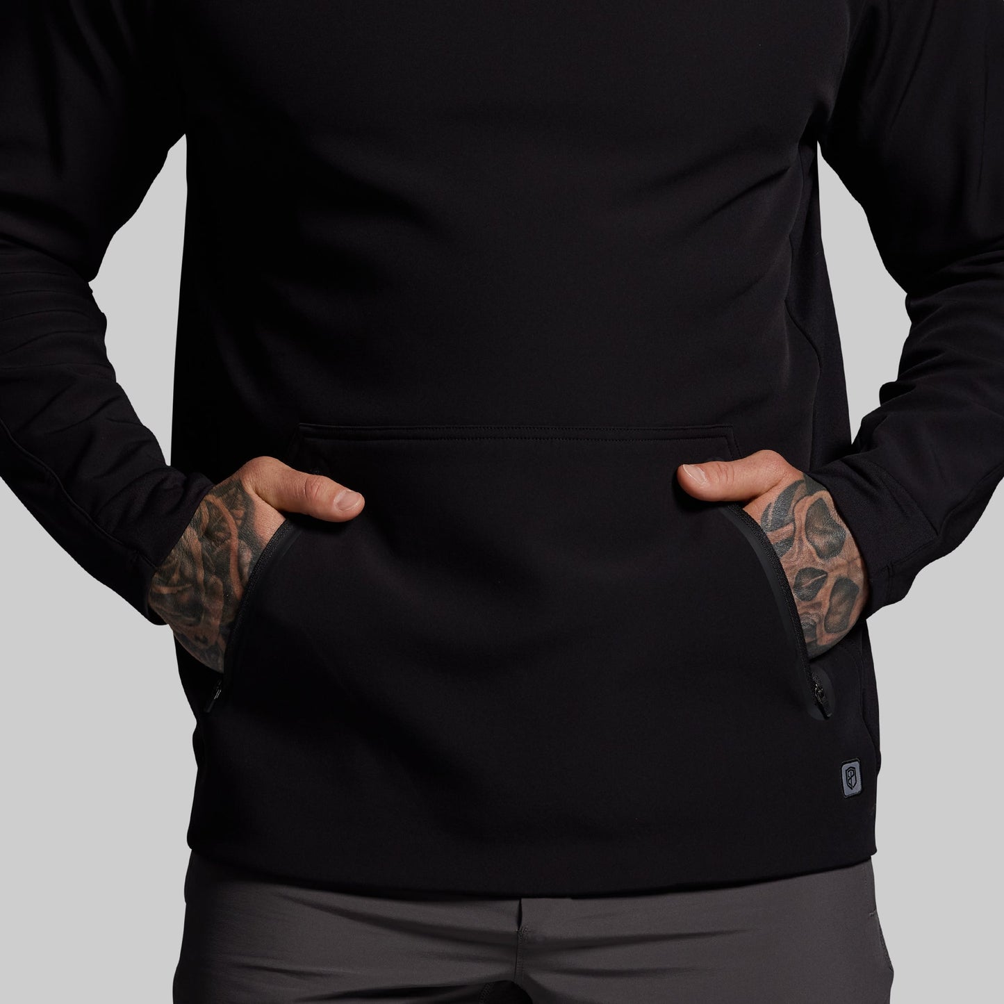 Person wearing a black jacket with tattoos on arms against a gray background