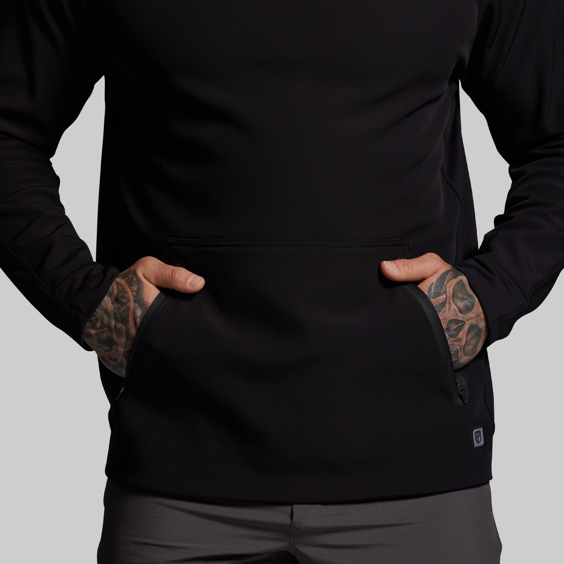 Person wearing a black jacket with tattoos on arms against a gray background