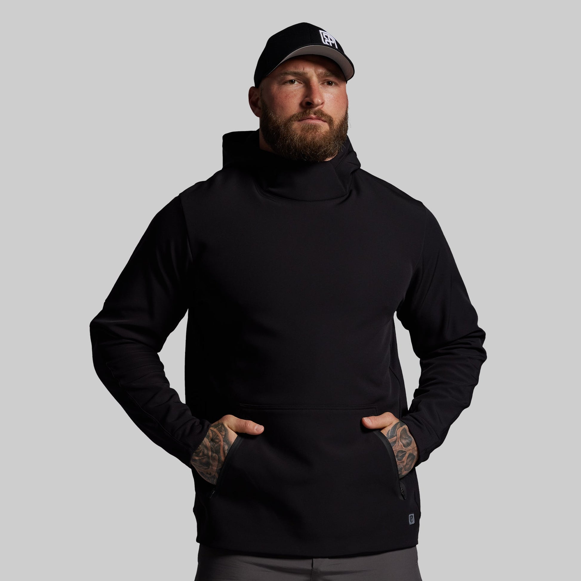 Man wearing a black hoodie and cap on a gray background