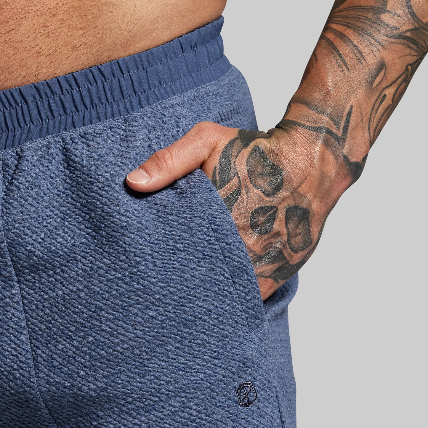 Person wearing blue shorts with a tattooed arm on a gray background