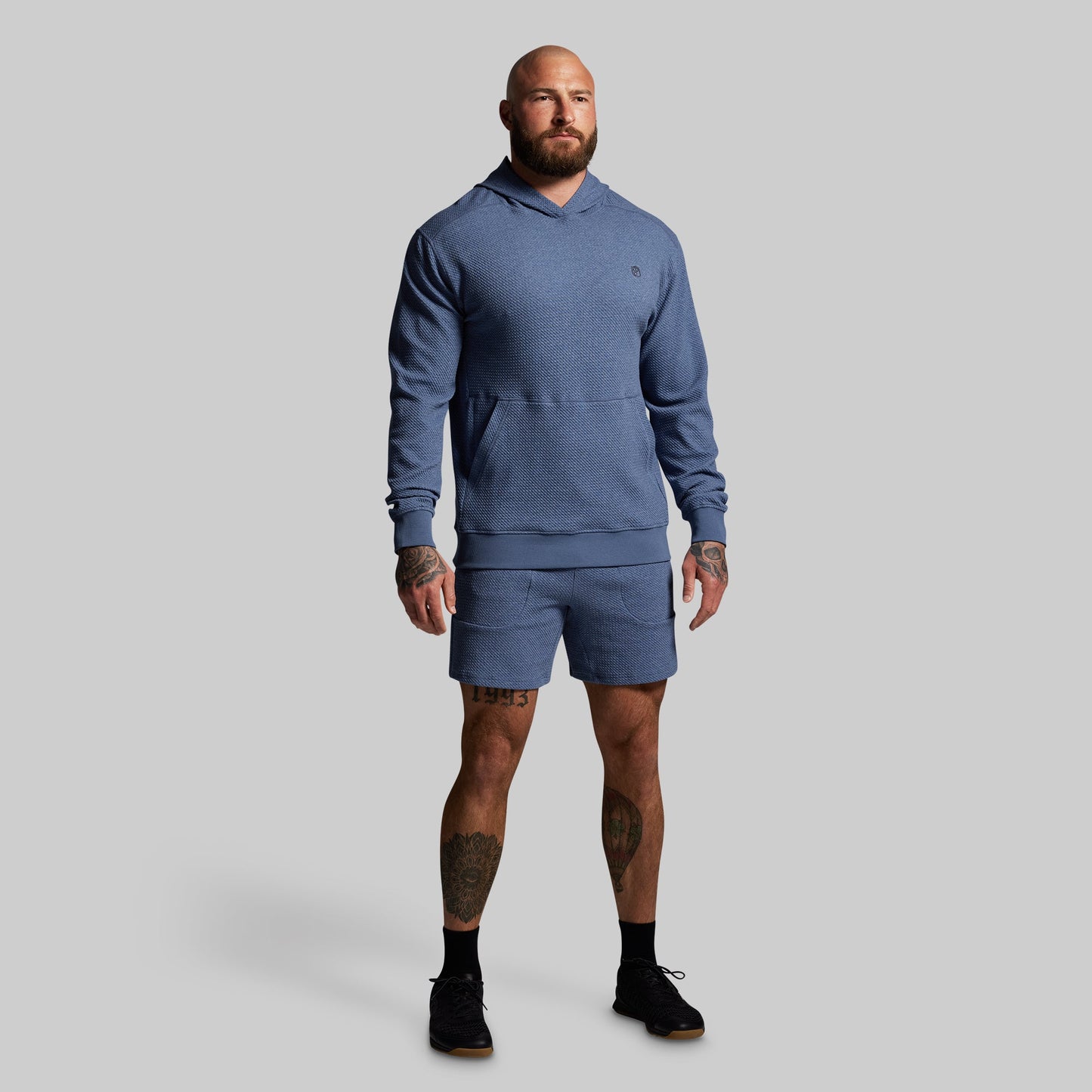 Man wearing a blue hoodie and shorts set on a gray background