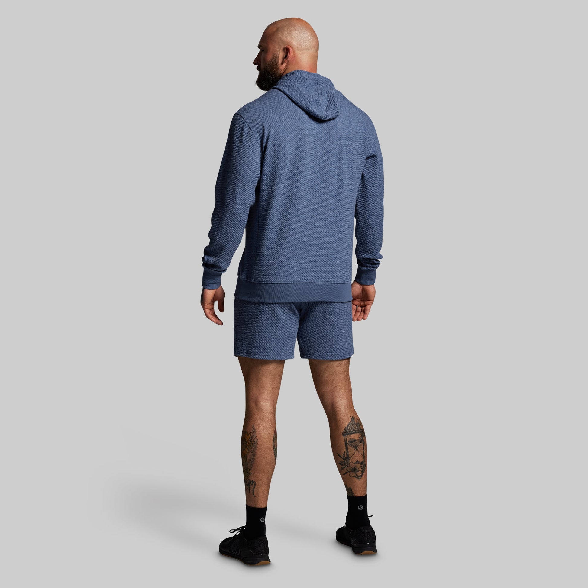 Man wearing a blue hoodie and shorts on a gray background