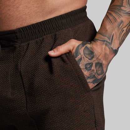 Brown textured shorts worn by a person with tattooed arm on a light gray background