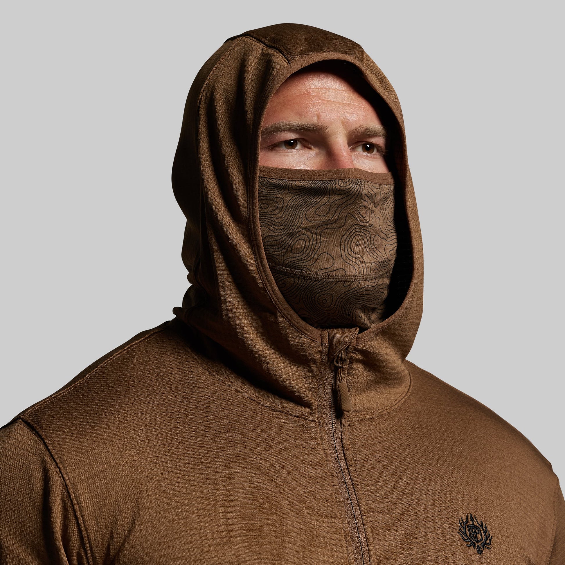Person wearing a brown hoodie with a face mask on a gray background