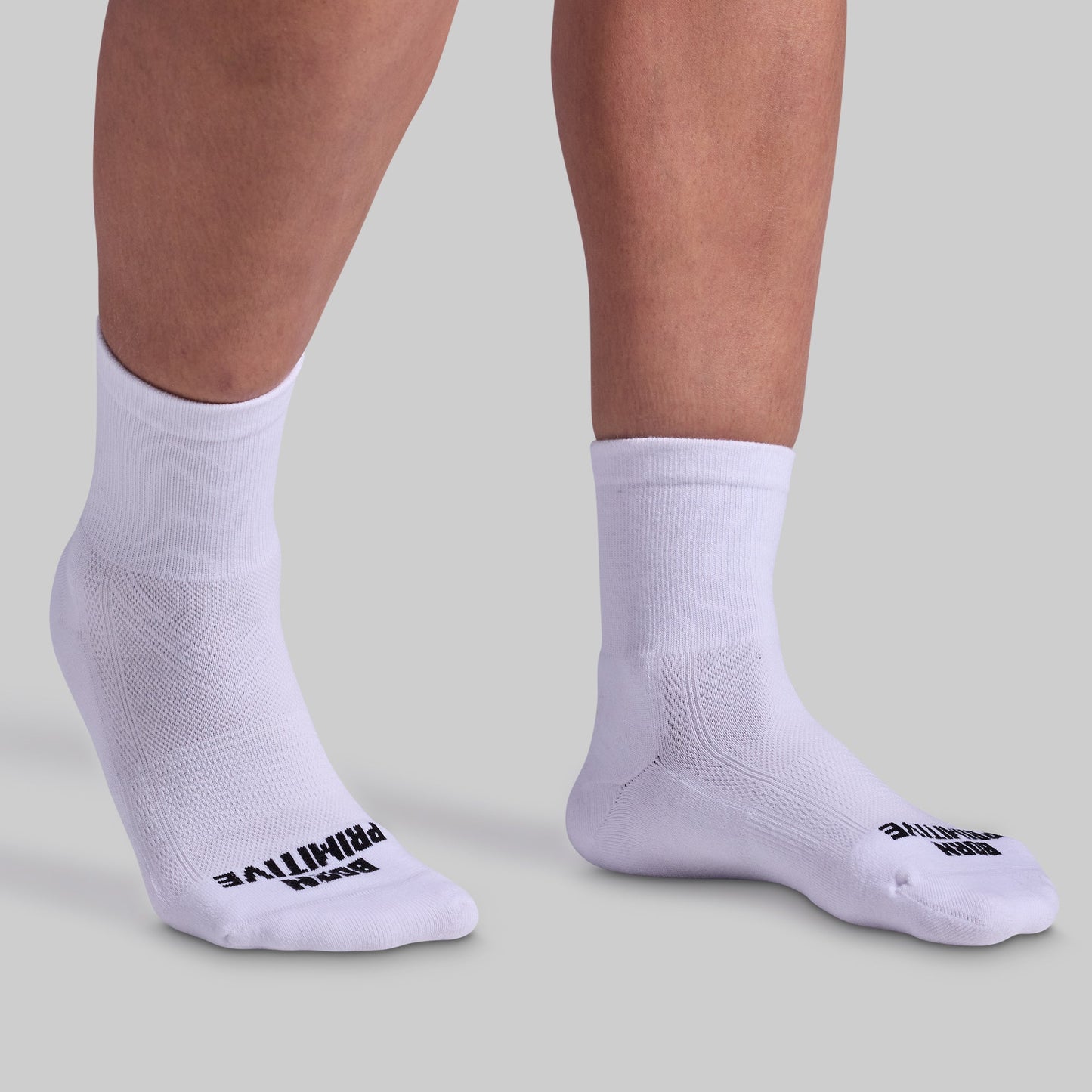 A pair of white, half crew socks with cushioned panels, displayed on a pair of legs. The socks have black text branding on the side.