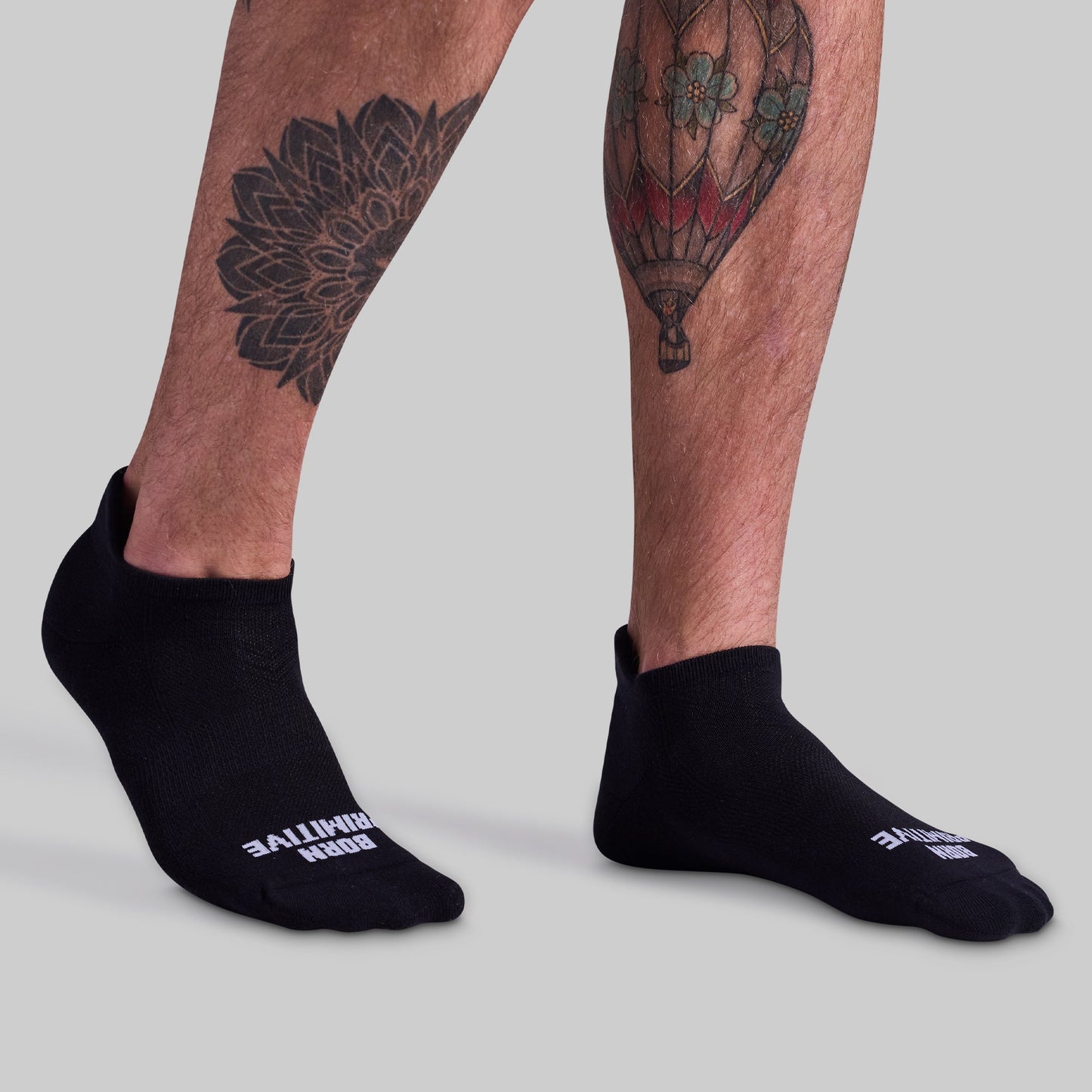 A pair of black ankle socks with cushioned panels, featuring a discrete logo on the side, worn on human legs.