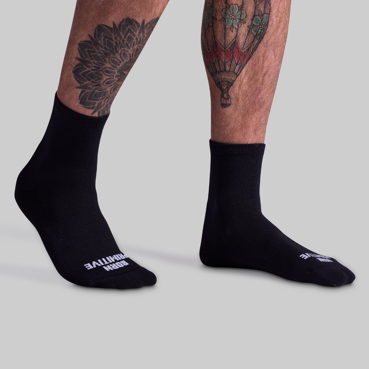 A pair of black performance half crew socks on a person's legs, showing the side profile with the brand name visible on the foot area.