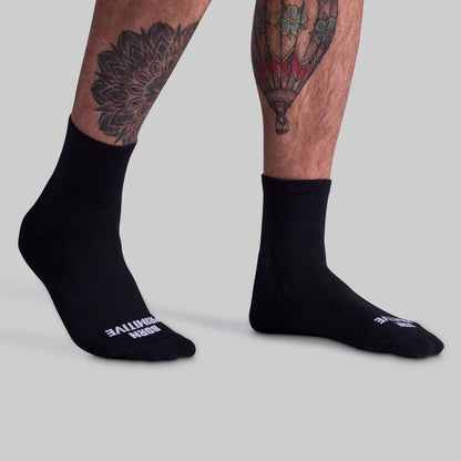 A pair of black performance half crew socks on a person's legs, showing the side profile with the brand name visible on the foot area.
