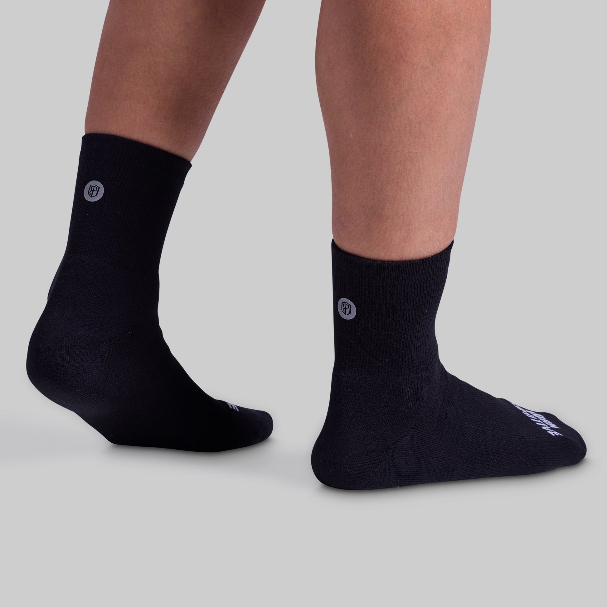 A pair of black performance half crew socks featuring a cushioned panel, displayed on a person's lower legs and feet.