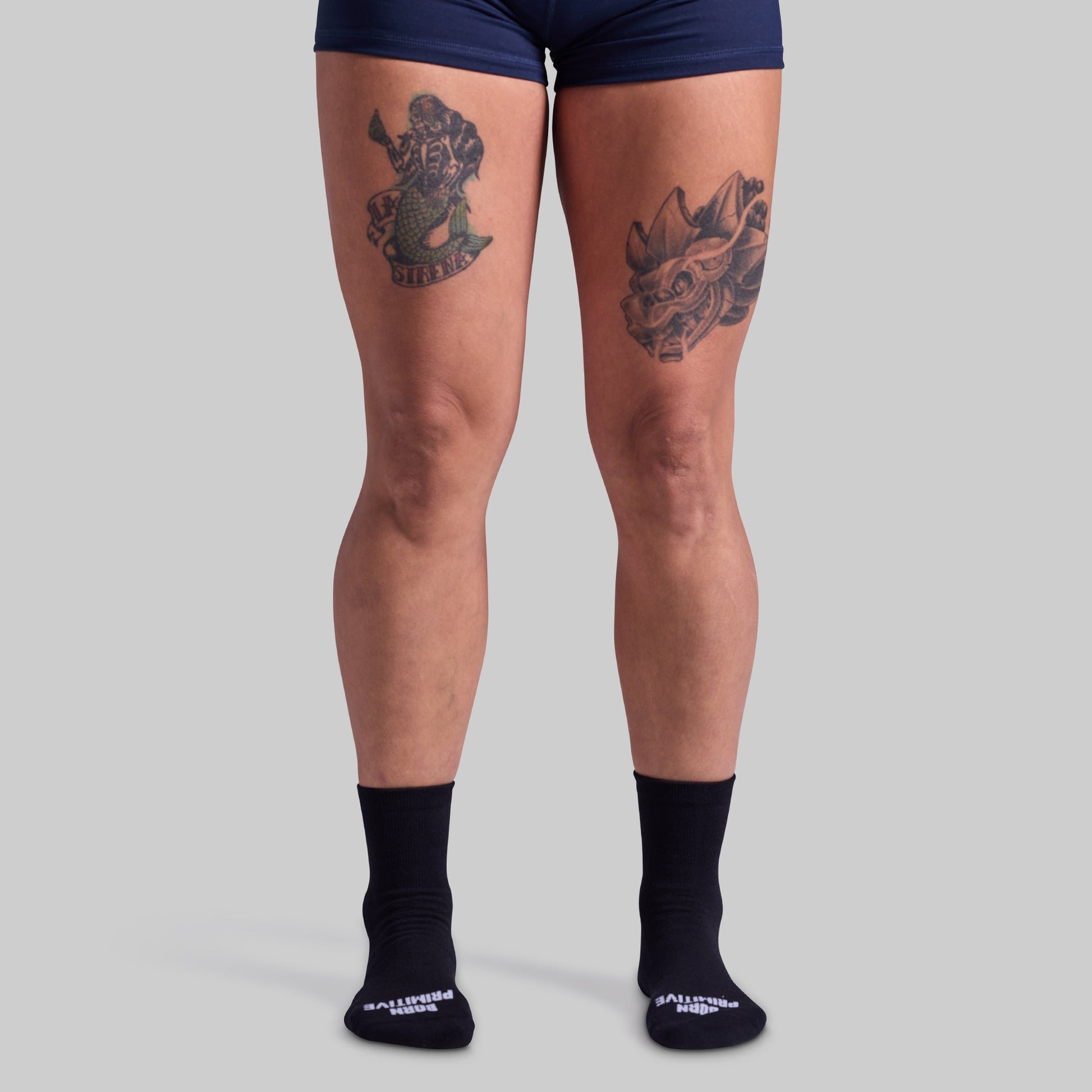 Person wearing navy blue shorts and black socks with visible tattoos on a gray background