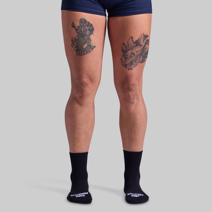 Person wearing navy blue shorts and black socks with visible tattoos on a gray background