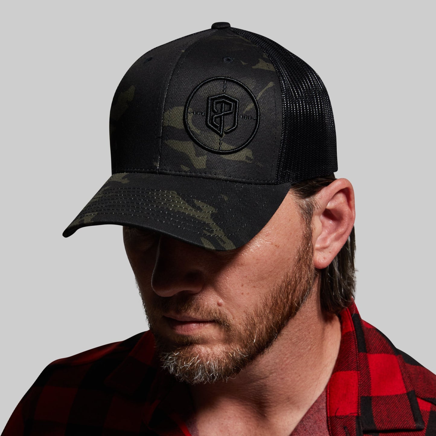 Man wearing a black camouflage baseball cap with a logo on a gray background