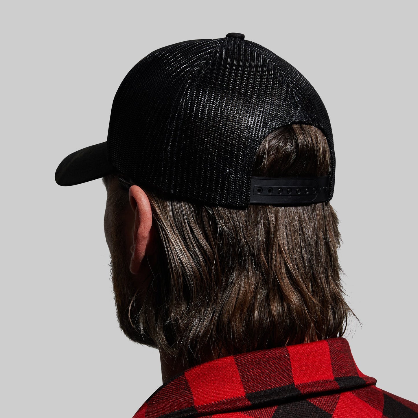 Person wearing a black mesh cap and red plaid shirt on a gray background