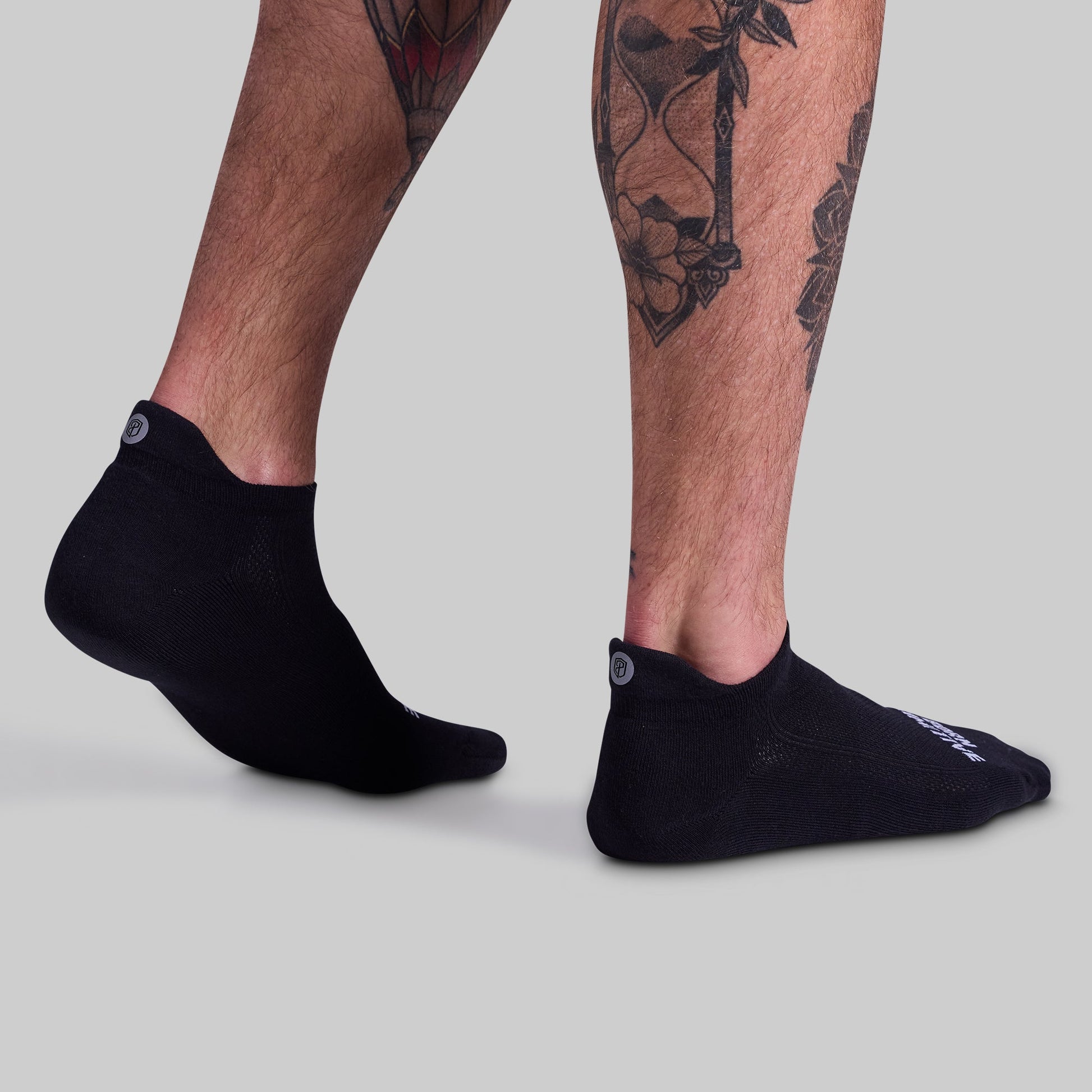 Black ankle socks worn by a person with tattoos on a light gray background