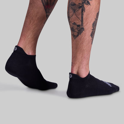 Black ankle socks worn by a person with tattoos on a light gray background