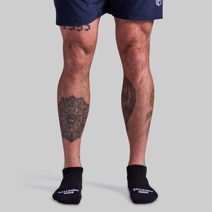 Person wearing navy shorts and black socks with visible tattoos on legs against a gray background
