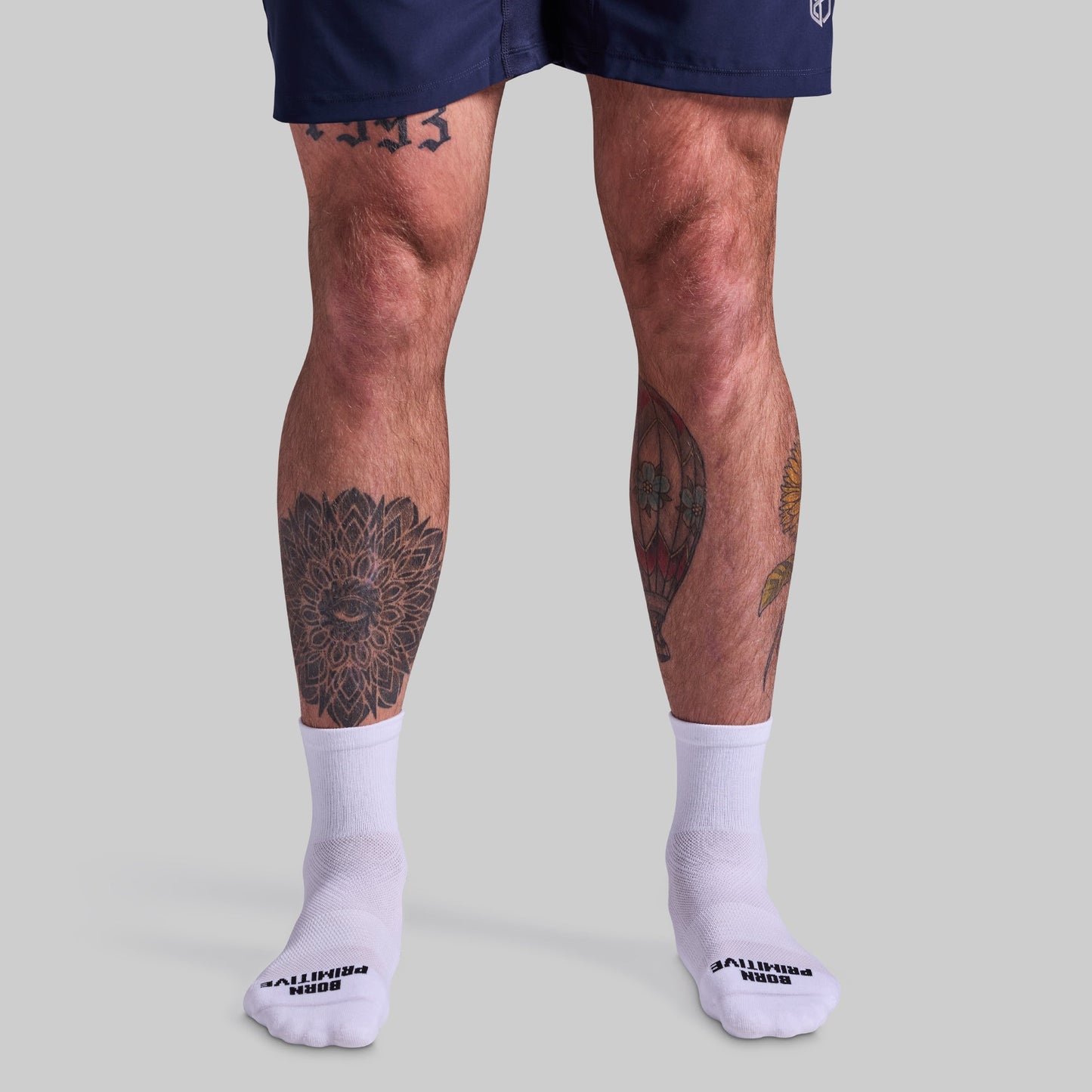 Person wearing navy shorts and white socks with visible tattoos on legs against a gray background