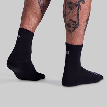 Black socks worn by a person with tattoos on a light gray background