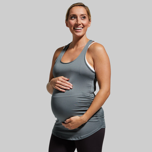 Pregnant woman wearing a gray tank top against a plain background