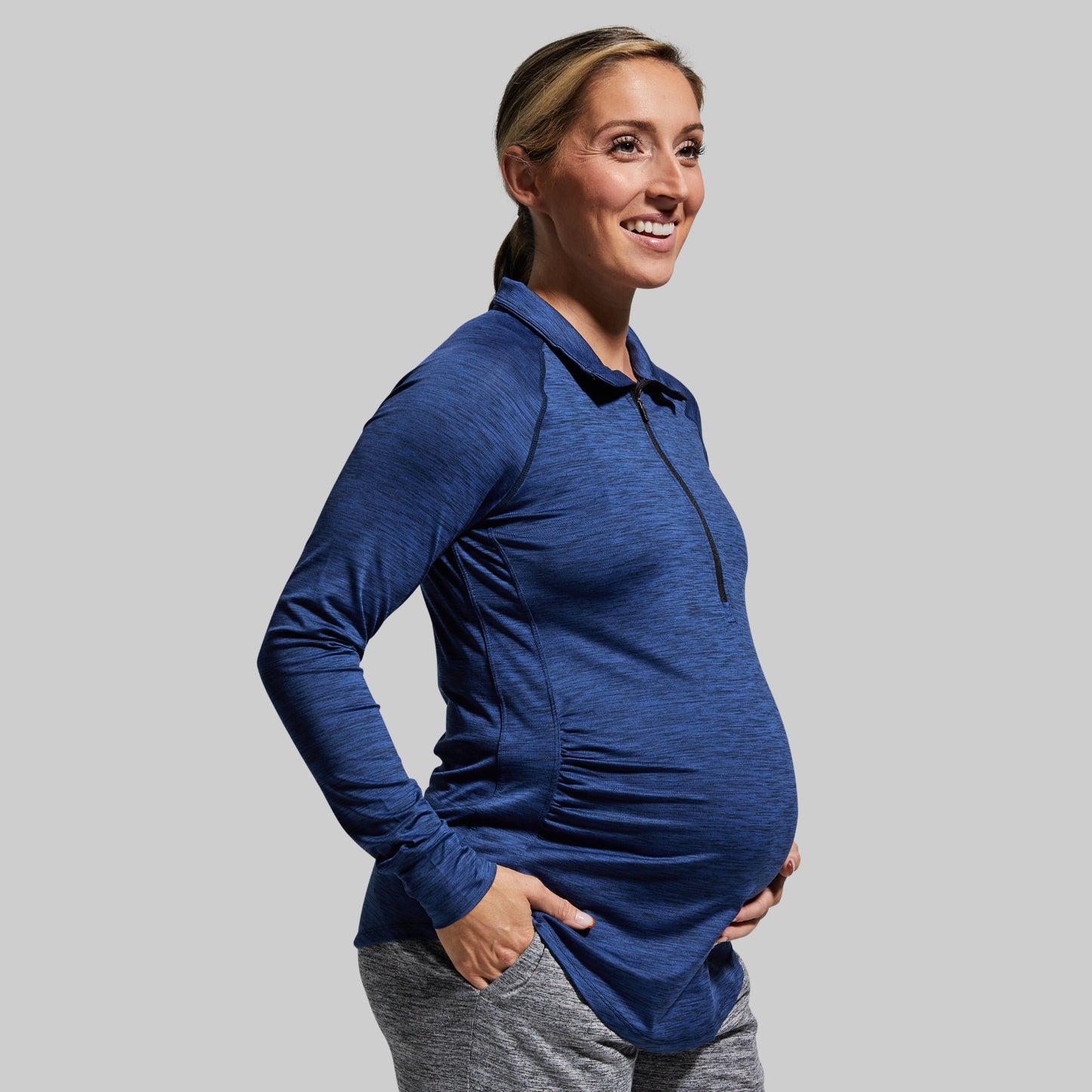 A pregnant woman wearing a navy blue long sleeve maternity shirt with a half zipper and hood.