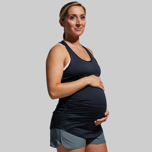 Pregnant woman wearing a black tank top and gray shorts against a plain background