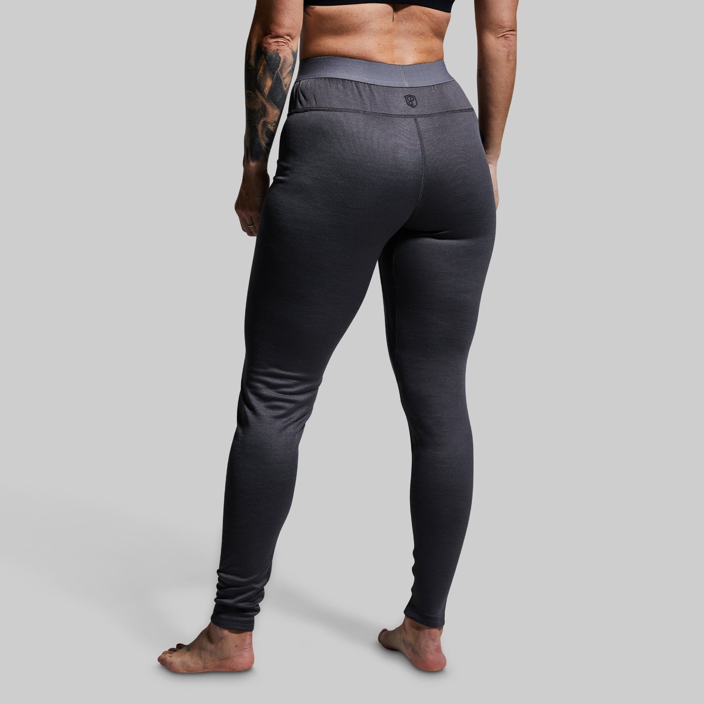 Woman wearing gray heavy base layer bottoms on a plain background