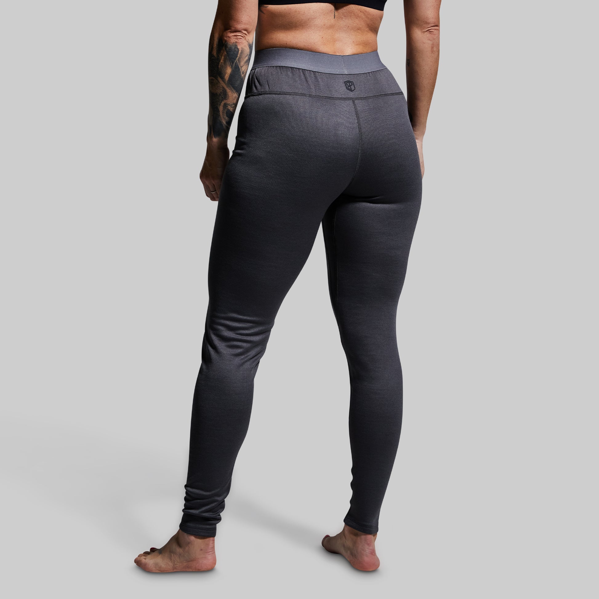 Woman wearing gray heavy base layer bottoms on a plain background