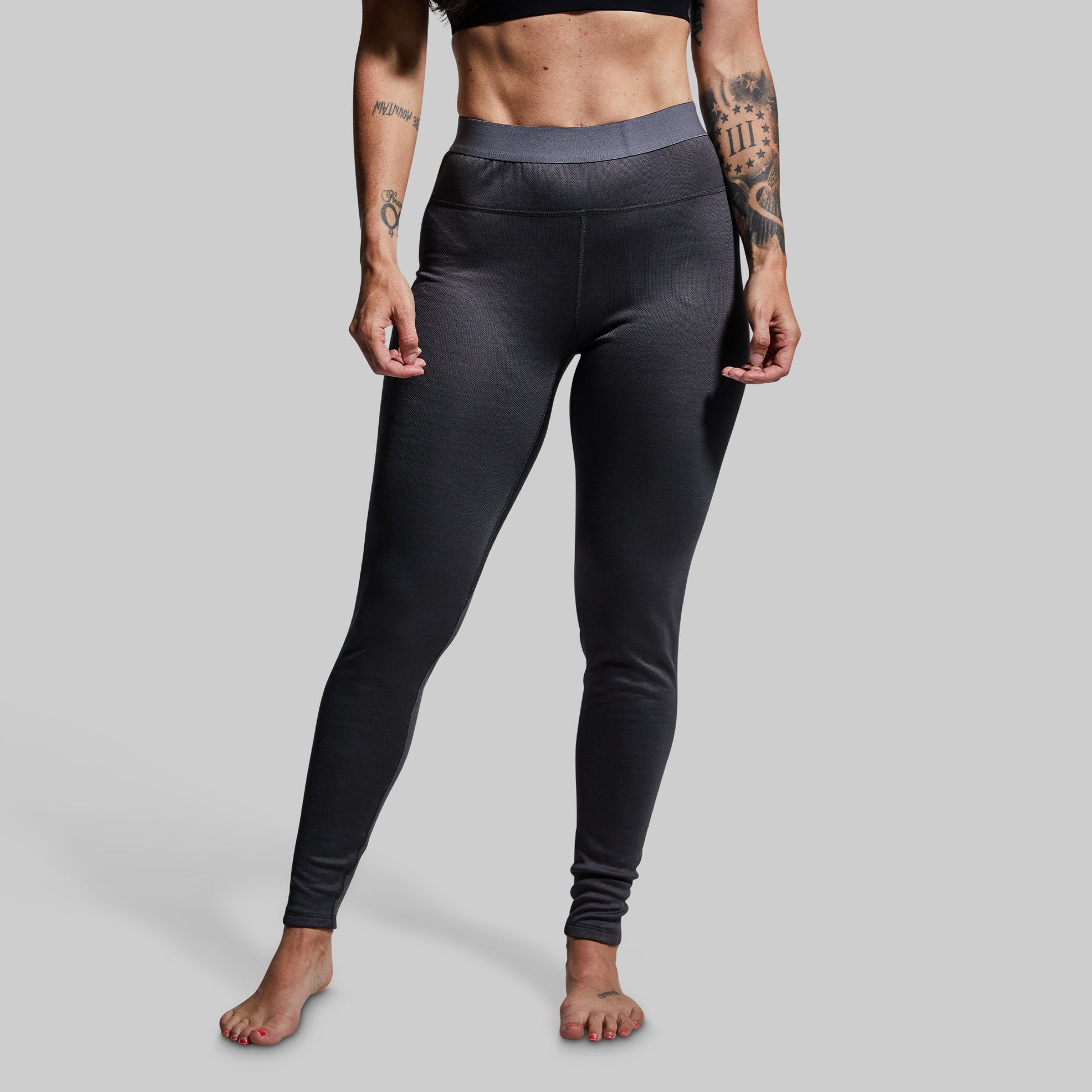 Woman wearing gray heavy base layer bottoms on a plain background