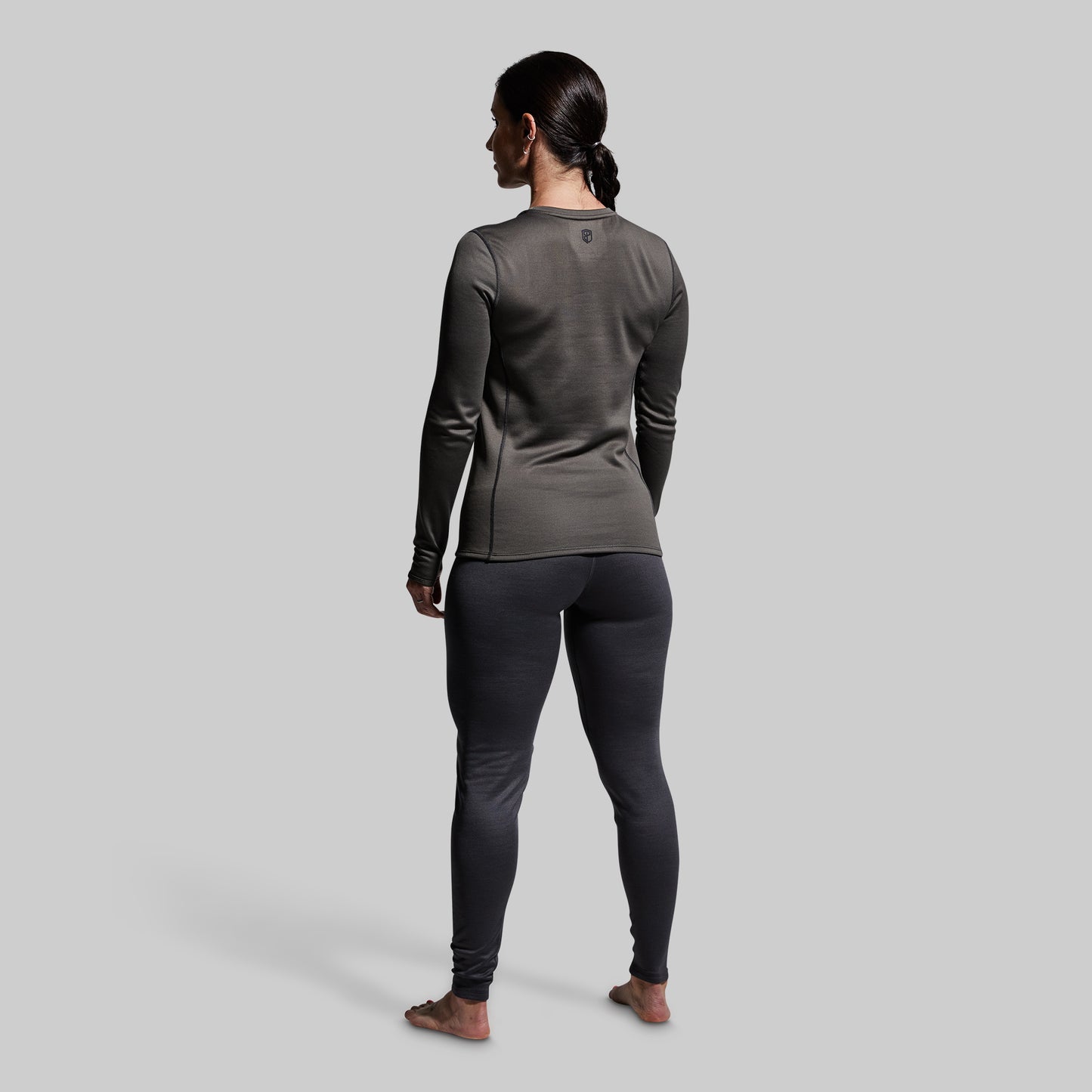 Woman wearing gray heavy base layer bottoms and long sleeve top on a plain background