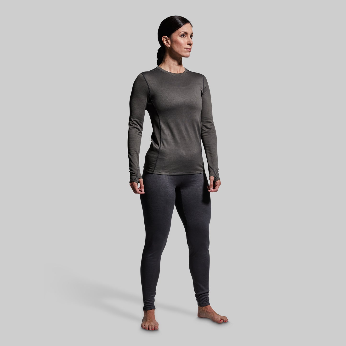 Woman wearing gray heavy base layer bottoms and long sleeve top on a plain background