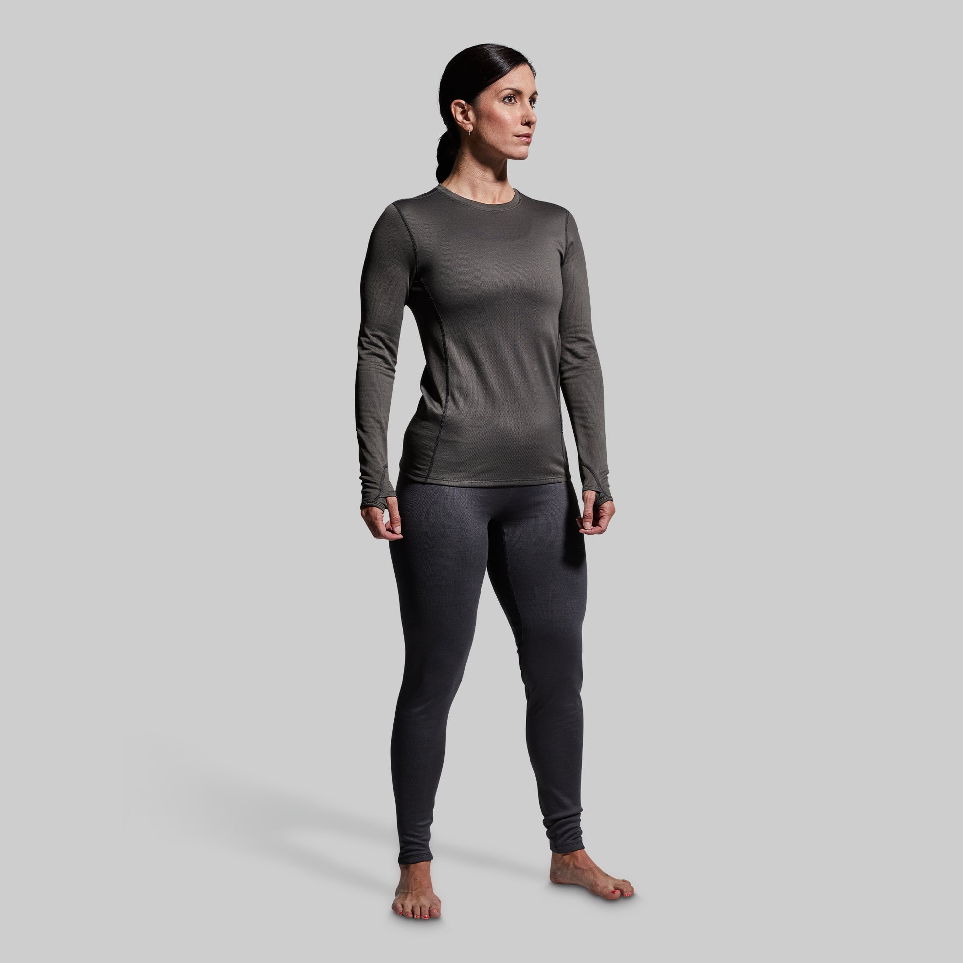 Woman wearing gray heavy base layer bottoms and long sleeve top on a plain background