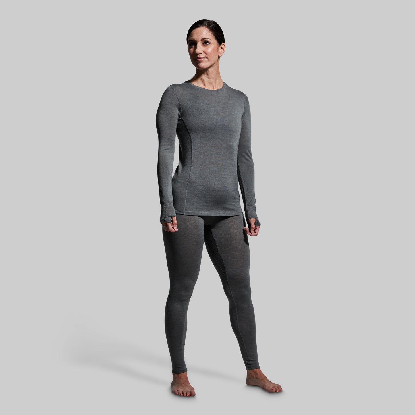 Woman wearing gray base layer bottoms and long sleeve top on a plain background