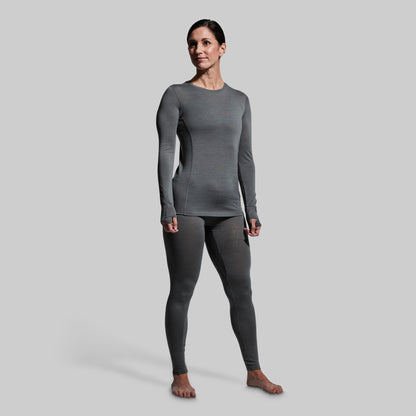 Woman wearing gray base layer bottoms and long sleeve top on a plain background