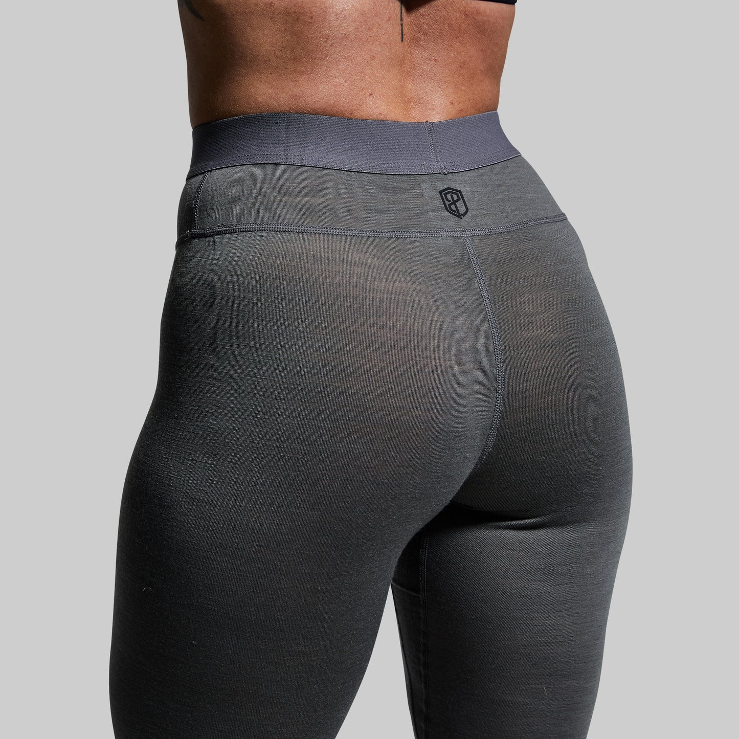 Close-up of a person wearing gray base layer bottoms on a plain background