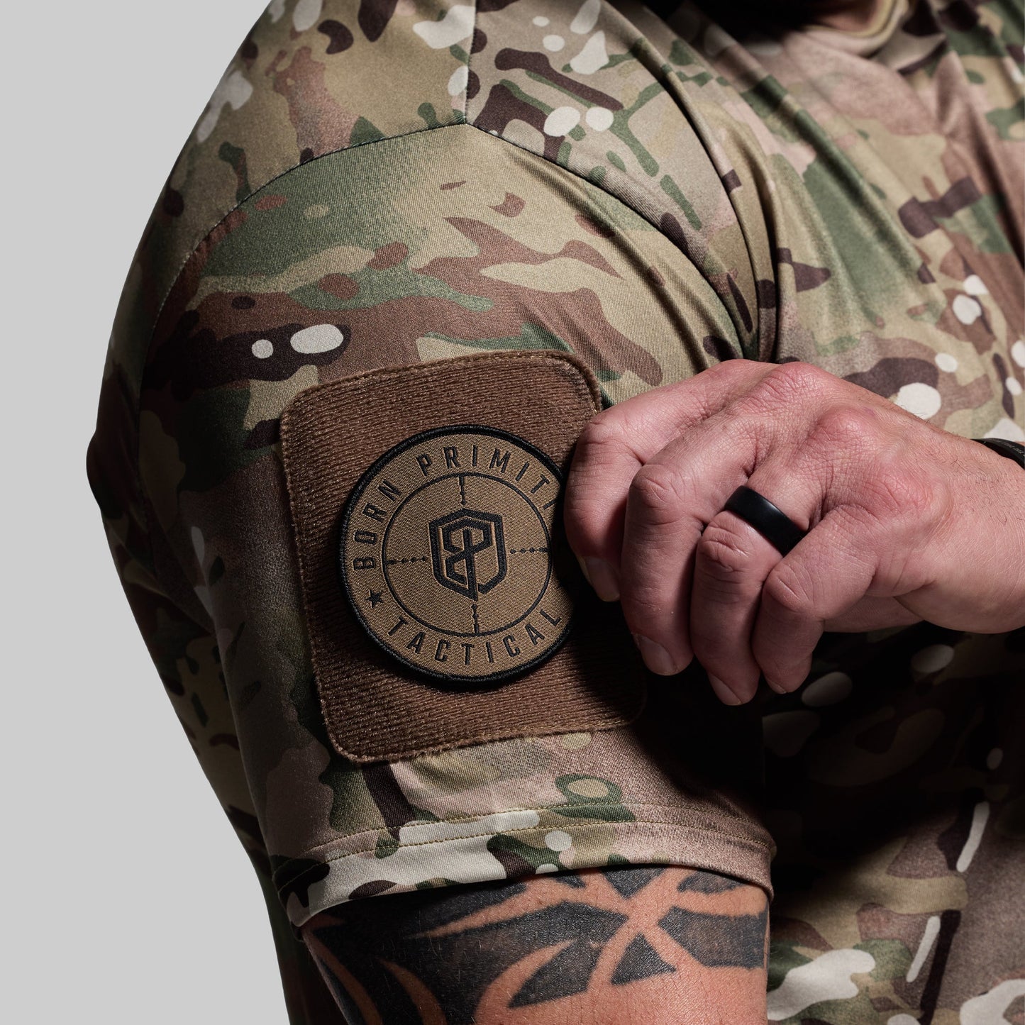 Person wearing a camouflage shirt with a 'Born Primitive Tactical' patch on a gray background