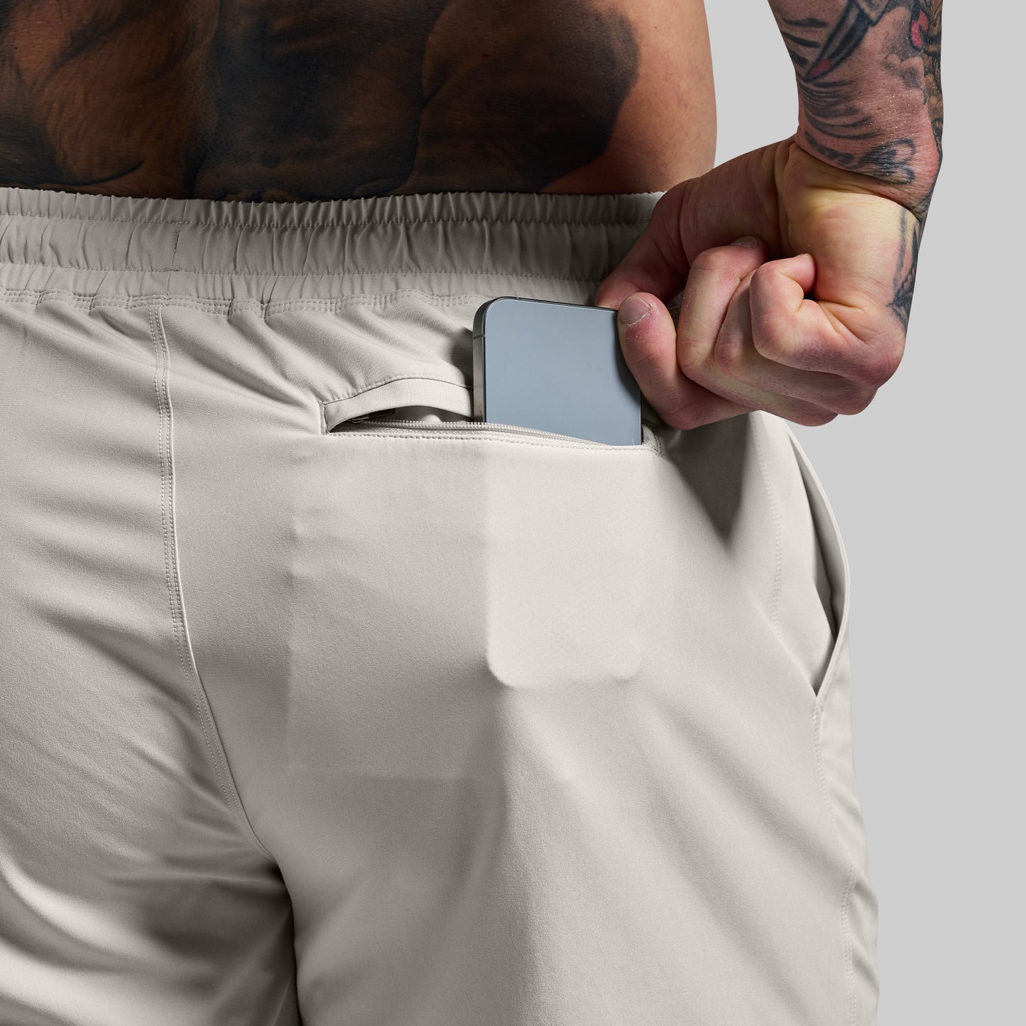 Person wearing beige shorts with a phone in the pocket against a plain background
