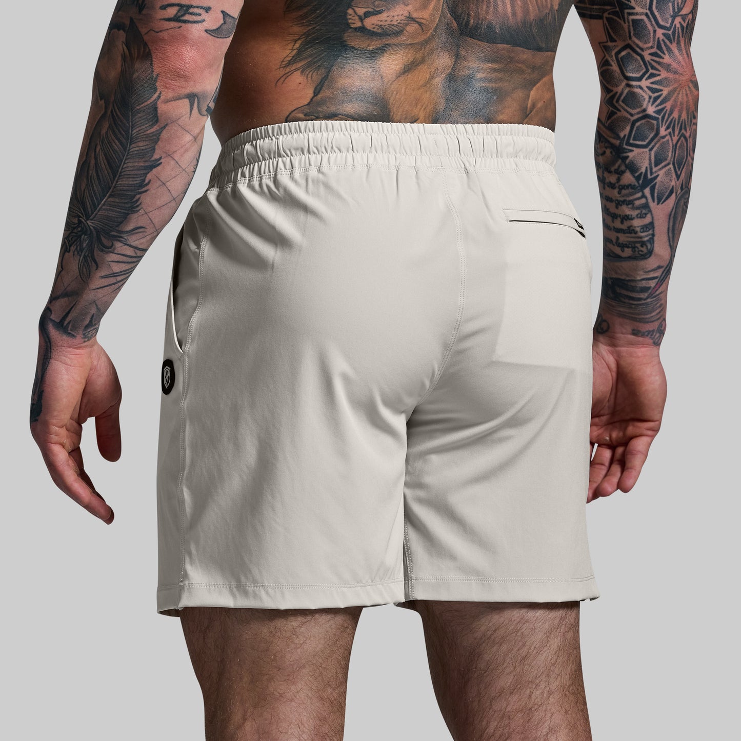 Beige shorts worn by a person with tattoos on a plain background
