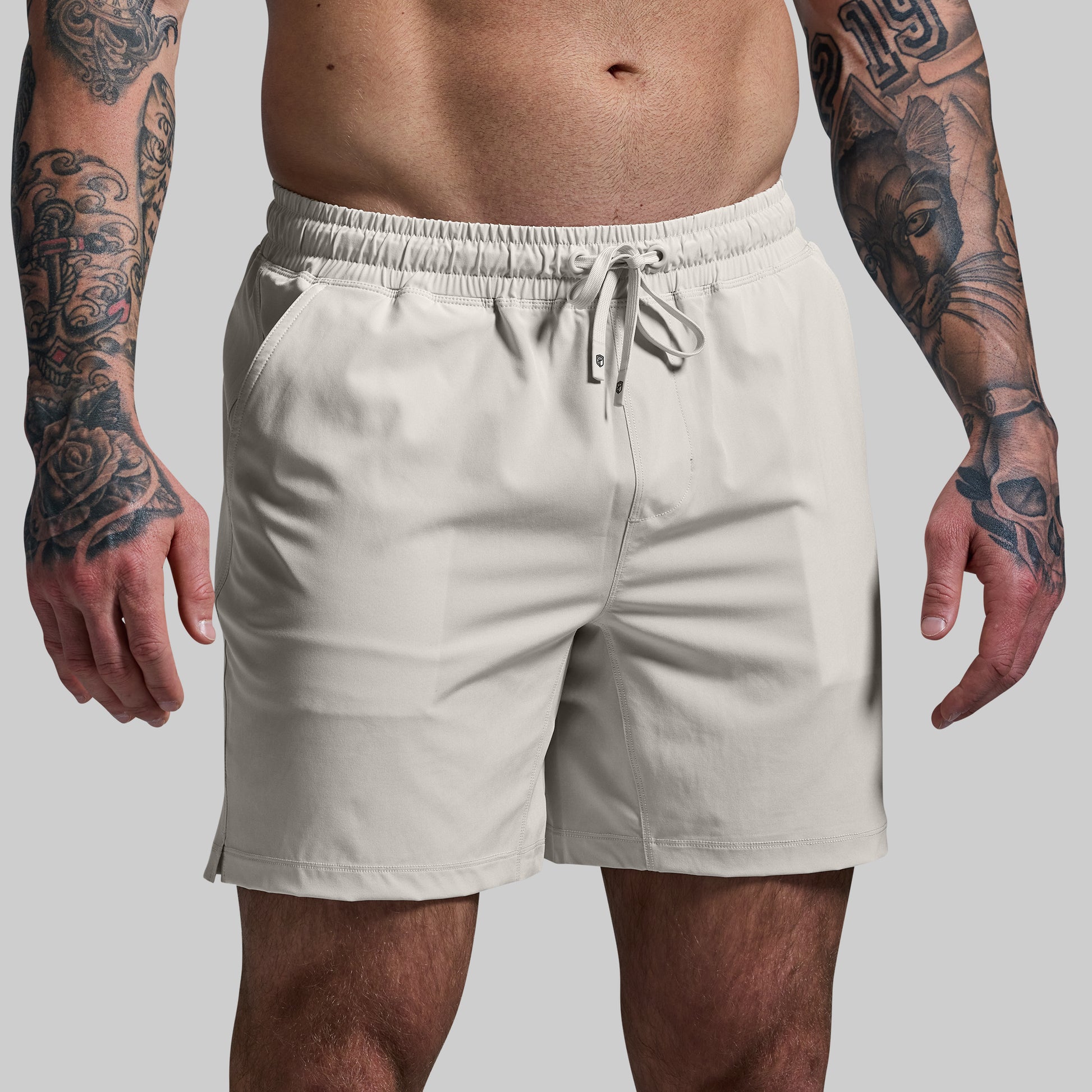 Beige shorts worn by a person with tattoos on a plain background