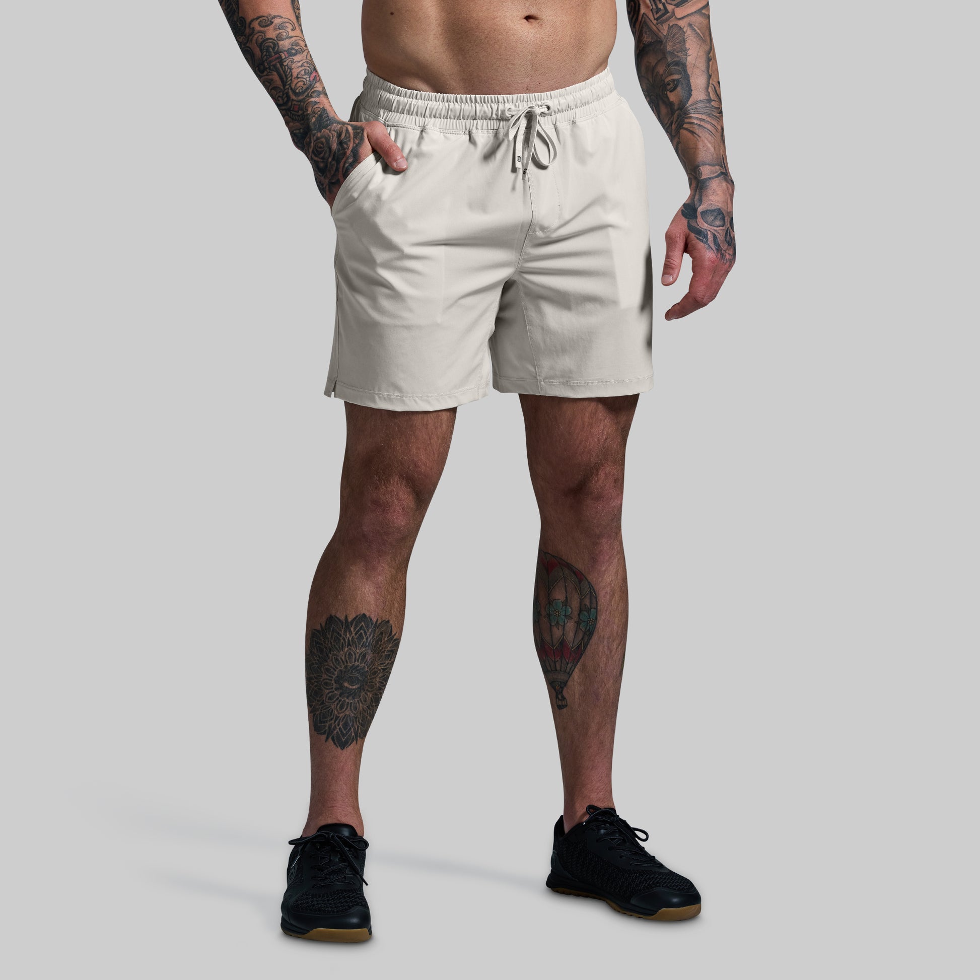 Person wearing beige shorts with tattoos on arms and legs against a gray background