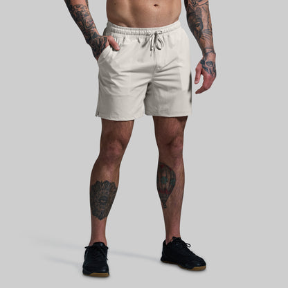 Person wearing beige shorts with tattoos on arms and legs against a gray background