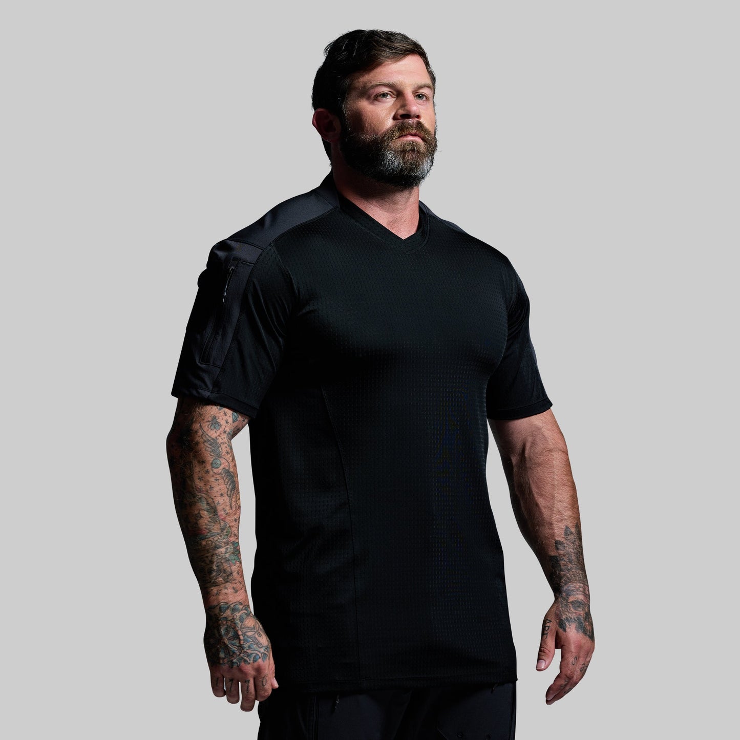 Man wearing a black tactical shirt against a gray background