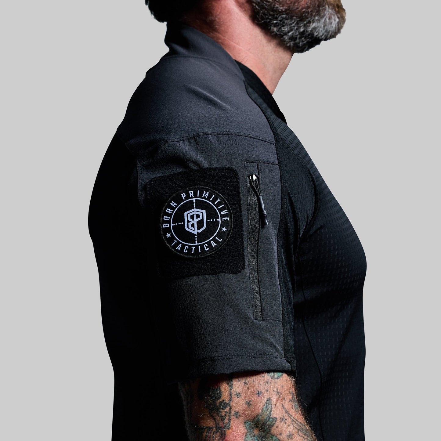 Person wearing a black tactical shirt with a visible brand logo on the sleeve against a gray background