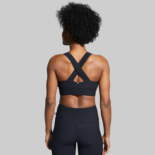 Person wearing a black sports bra with criss-cross straps on a gray background