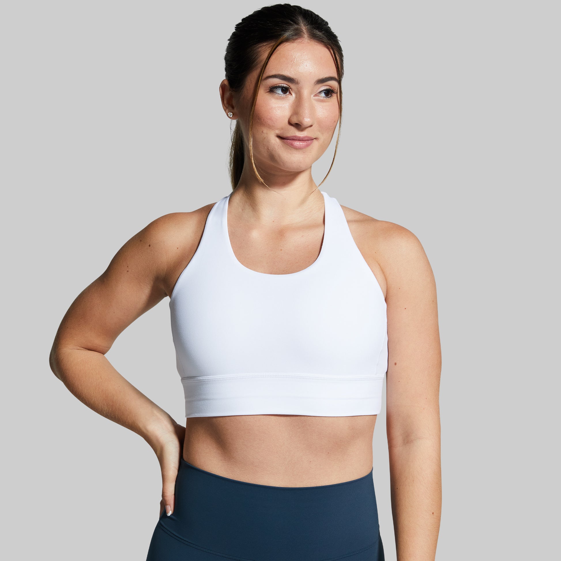 Woman wearing a white sports bra and navy leggings on a gray background