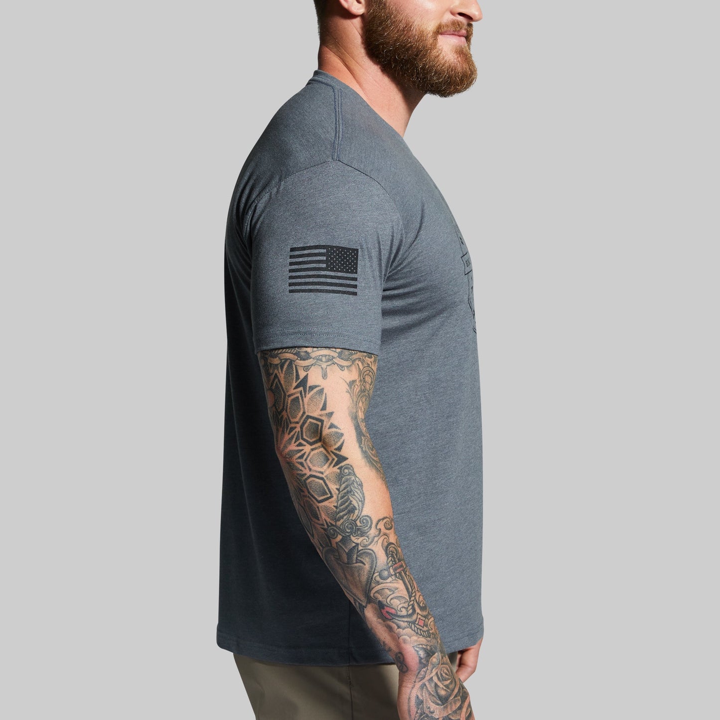 Man wearing a gray t-shirt with a tattooed arm on a plain background